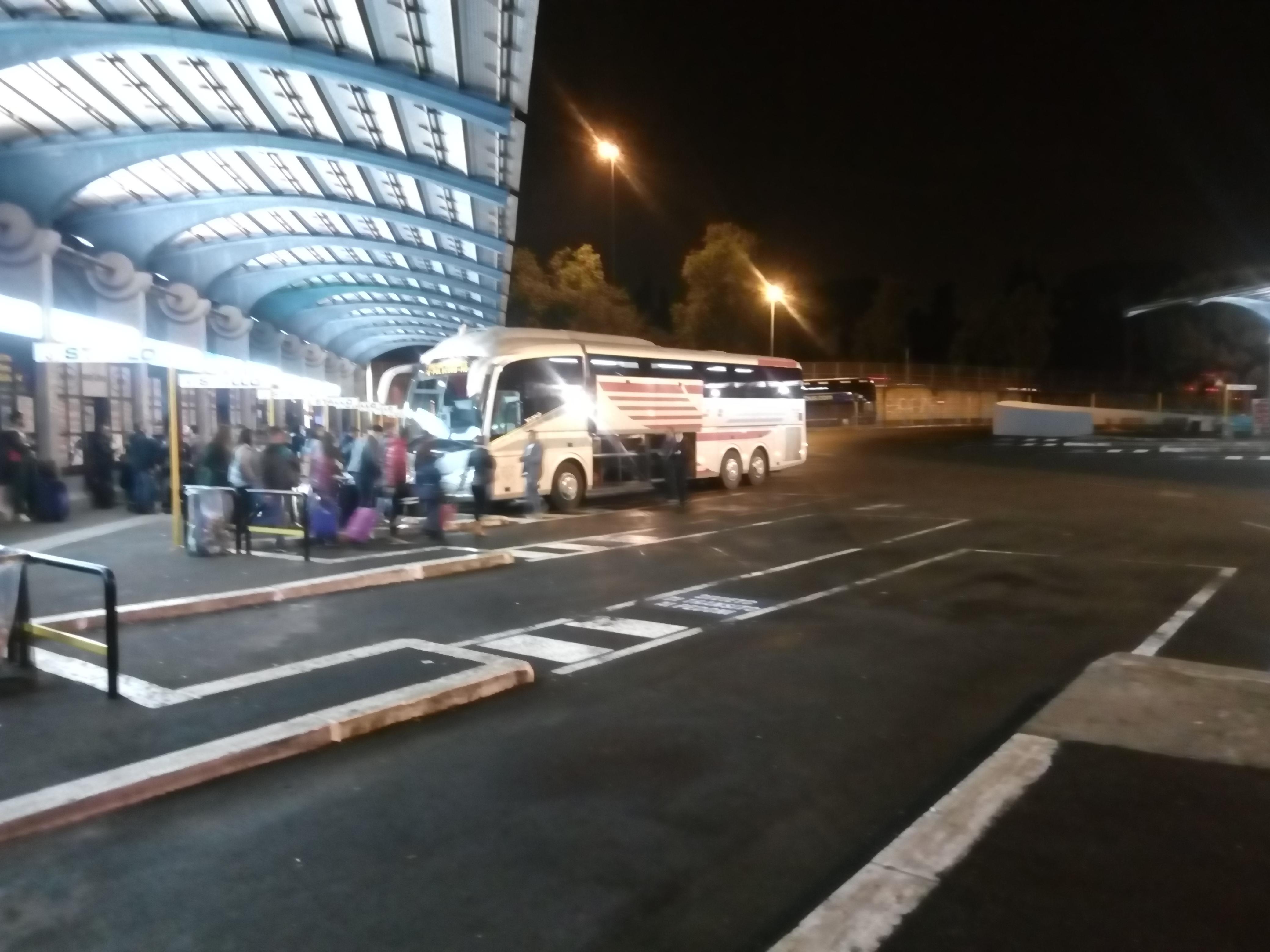 夜の大型バスターミナルに停まるバスと乗客たち